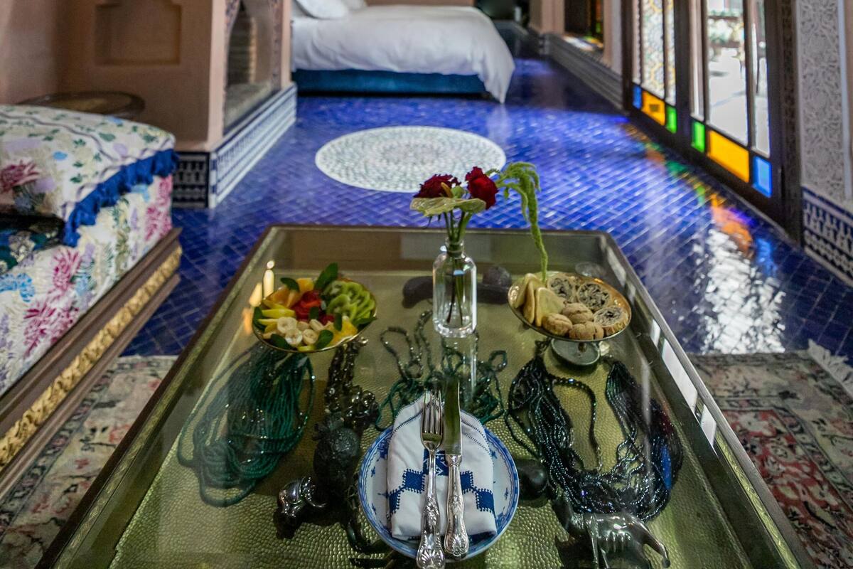 A room with a bed, a tray with decorative items, and a view through a stained glass window.