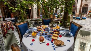 Un área de comedor al aire libre con una mesa lista para el desayuno, rodeada de follaje y decoración tradicional.