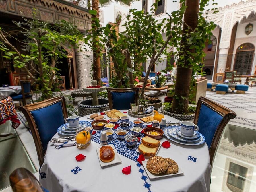 Un área de comedor al aire libre con una mesa lista para el desayuno, rodeada de follaje y decoración tradicional.