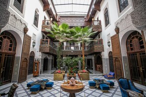 A spacious courtyard with ornate architecture, a central seating area, and a lush green garden. - Riad Semlalia (Fes)