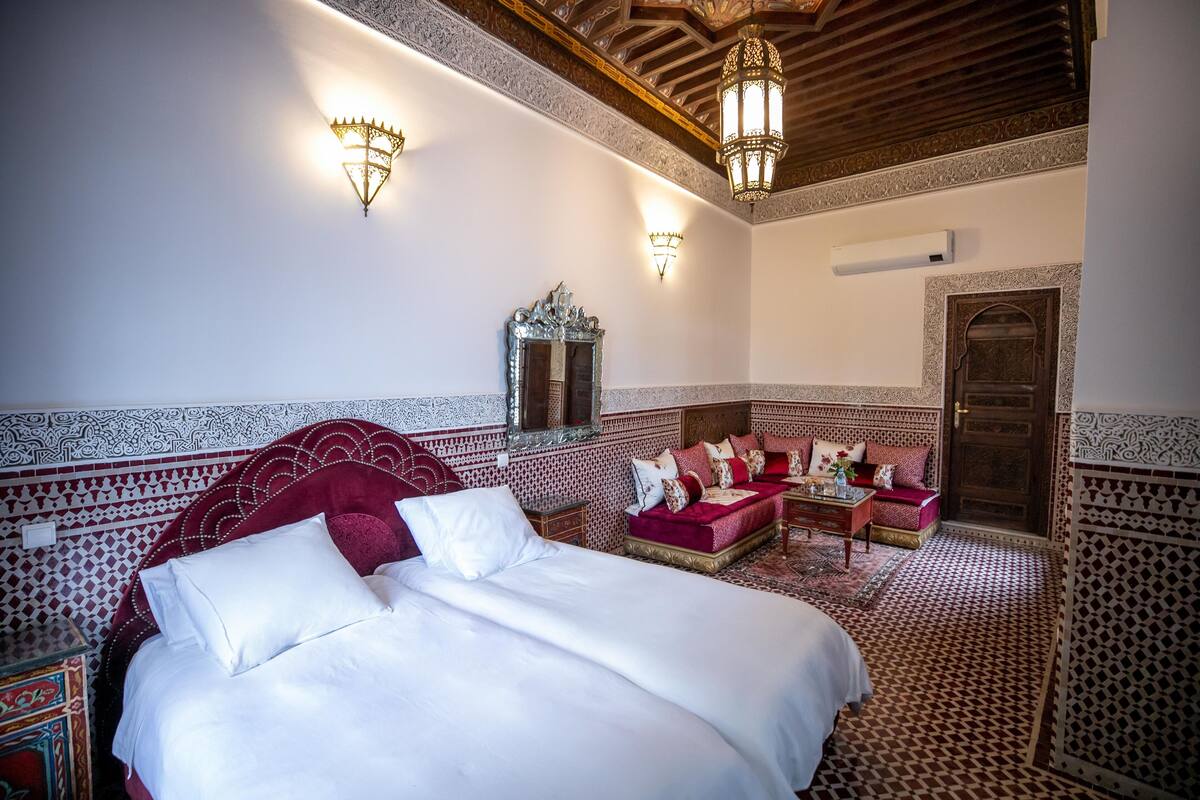 A traditional Moroccan room with a large bed, a sofa set, and decorative wall sconces.