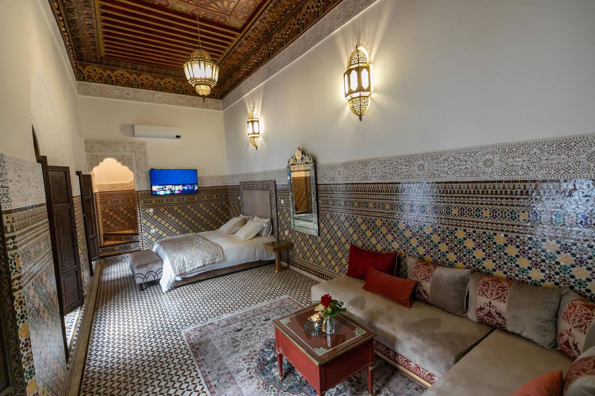 A traditional Moroccan room with a bed, sofa, and TV.