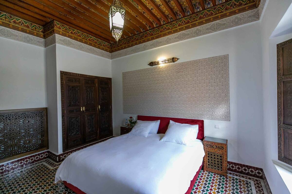 A room with a large bed, wooden ceiling, patterned walls, and a decorative door.
