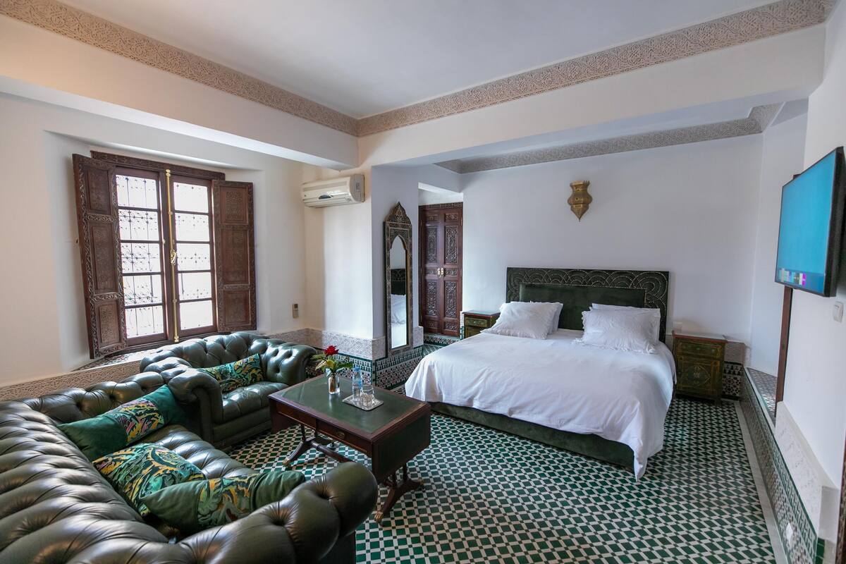 A room with a large bed, a leather sofa, and a small table.