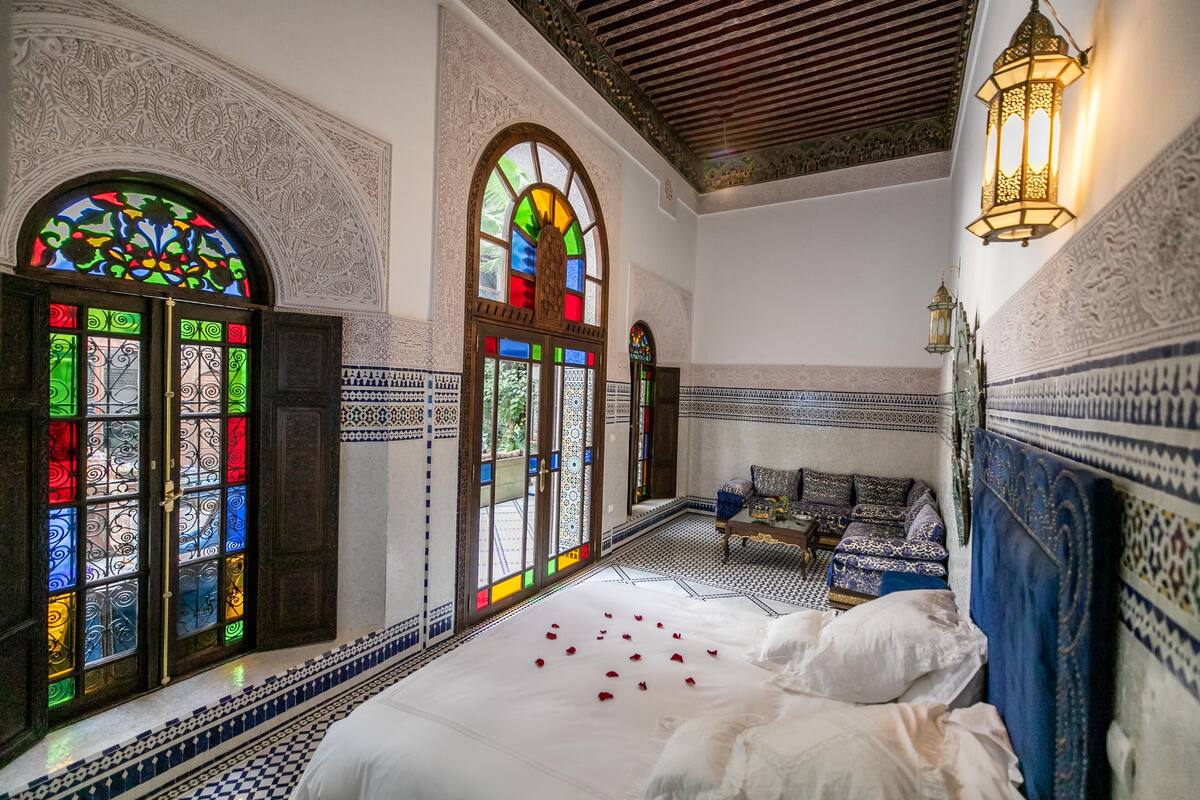 A room with intricate tile work, a bed with rose petals, and a bench.