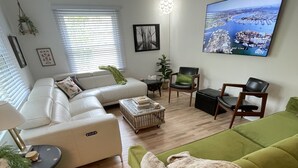 A living room with a green sofa, a white sofa, a coffee table, and a TV mounted on the wall. - Spacious cottage by lake & walking trails, 1 mile from downtown Shipshe. (Shipshewana)