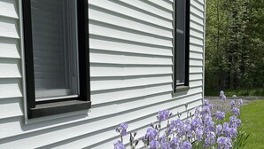 A white house with black window frames and a garden with purple flowers. - Spacious cottage by lake & walking trails, 1 mile from downtown Shipshe. (Shipshewana)