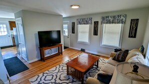 A living room with a TV on a stand, a wooden coffee table, a sofa, and patterned rugs. - Waterfront house on the upper most portion of the West Branch Delaware. (Deposit)