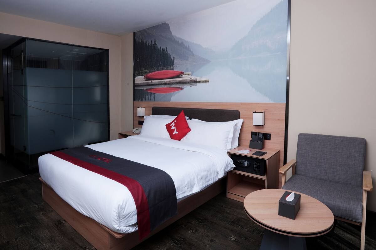 A hotel room with a bed, a bedside table with a lamp, a chair, and a round table.