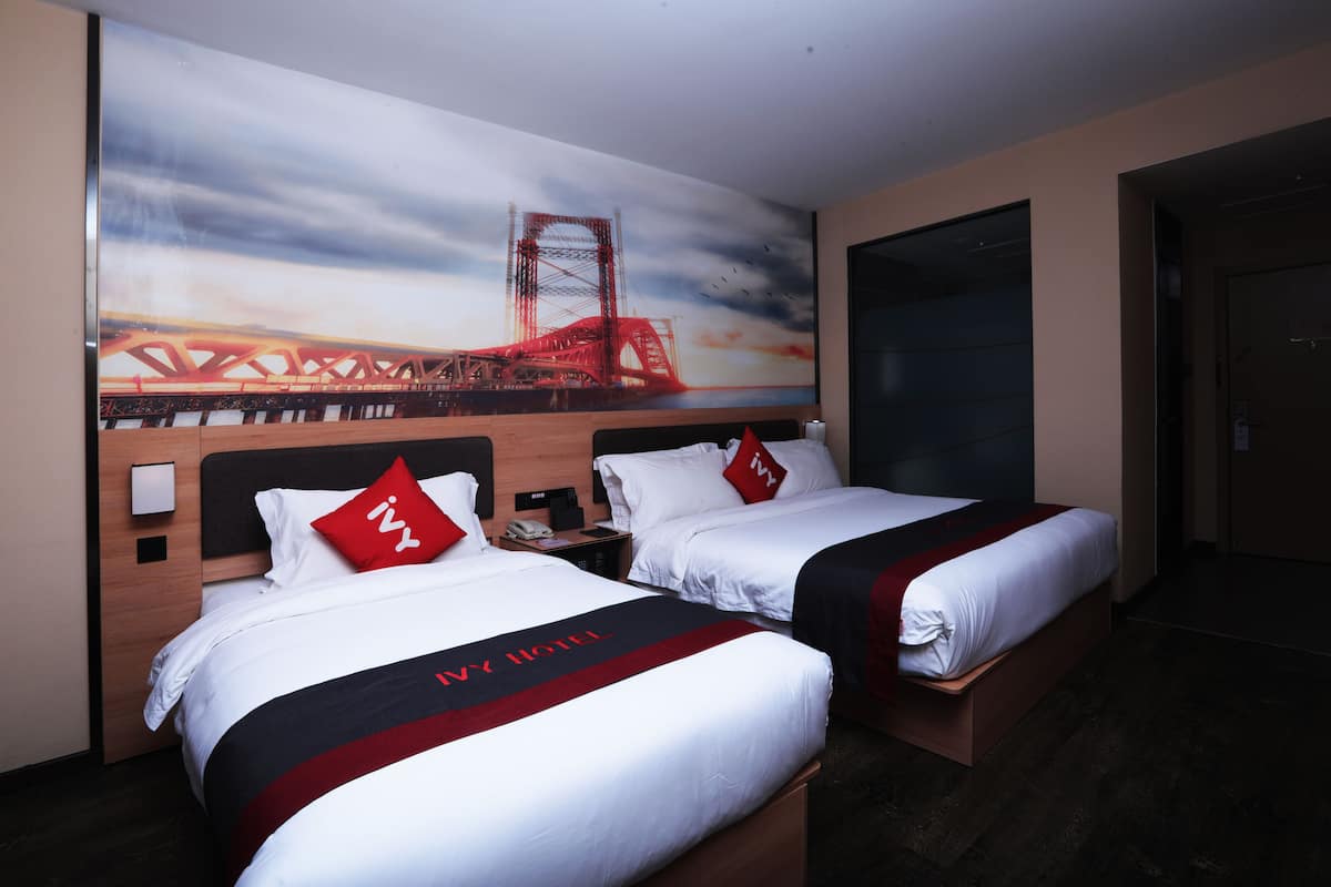 A hotel room with two beds, a large painting of a bridge, and a wooden headboard.
