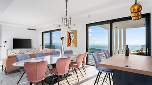 A modern living room with a large dining table, pink upholstered chairs, a sofa, and a large window offering a view of the sea. - Villa Sagnia, 4 en-suite bedrooms, sea views (Makarska)