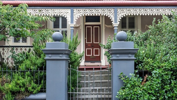 Une maison avec un toit rouge, une porte marron et un porche blanc décoratif.