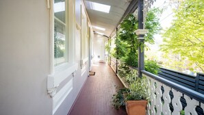 Un couloir couvert doté d’un sol carrelé, de murs blancs et d’une rambarde ornée de plantes.