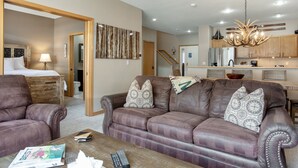 A living room with a brown leather sofa, a wooden coffee table, and a dining area with a chandelier.