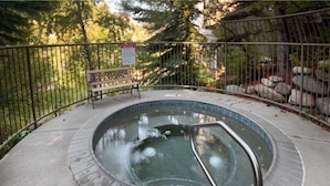 A hot tub with a metal railing, surrounded by a fence and trees.