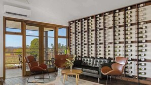 A room with a leather sofa, two brown chairs, a round wooden table, and a wall of wine bottles.