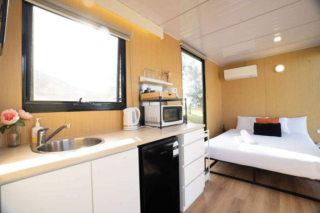Ein kleines Zimmer mit einem Bett, einem Waschbecken, einer Mikrowelle und einem kleinen Fenster.
