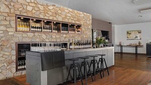 A bar area with a stone wall, shelves of bottles, glasses, and stools.