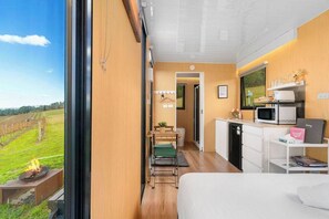 Une chambre à coucher comprenant un lit, un bureau, une chaise, une petite table avec une plante, et donnant sur un vignoble.