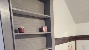 Un baño con un mueble estante integrado gris, una toalla colgada en la pared y suelo de madera.
