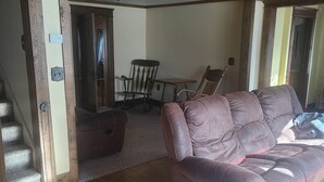 Una sala de estar con techo de madera, un sofá de cuero marrón, un tapete estampado y una zona de comedor con una mesa y sillas.