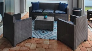 A covered outdoor seating area with a sofa, two armchairs, and a coffee table, featuring a patterned rug and a potted plant. - Casa Sanibel 3bed 2bth heated Pool home (Fort Myers)