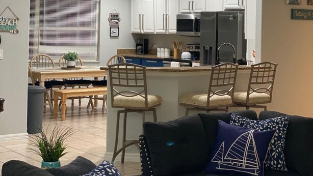 A modern kitchen with white cabinets, a central island with bar stools, and a dining area with a table and chairs. - Casa Sanibel 3bed 2bth heated Pool home (Fort Myers)