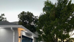 A residential property with a paved driveway, a blue garage door, and a small garden with colorful plants. - Casa Sanibel 3bed 2bth heated Pool home (Fort Myers)