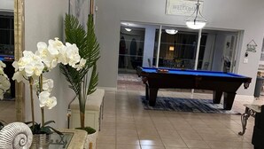 A pool table in a living room with a glass coffee table and potted plants. - Casa Sanibel 3bed 2bth heated Pool home (Fort Myers)
