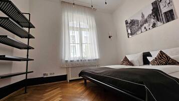 Un dormitorio con cama, una escalera, una ventana con cortinas translúcidas y un cuadro en la pared.