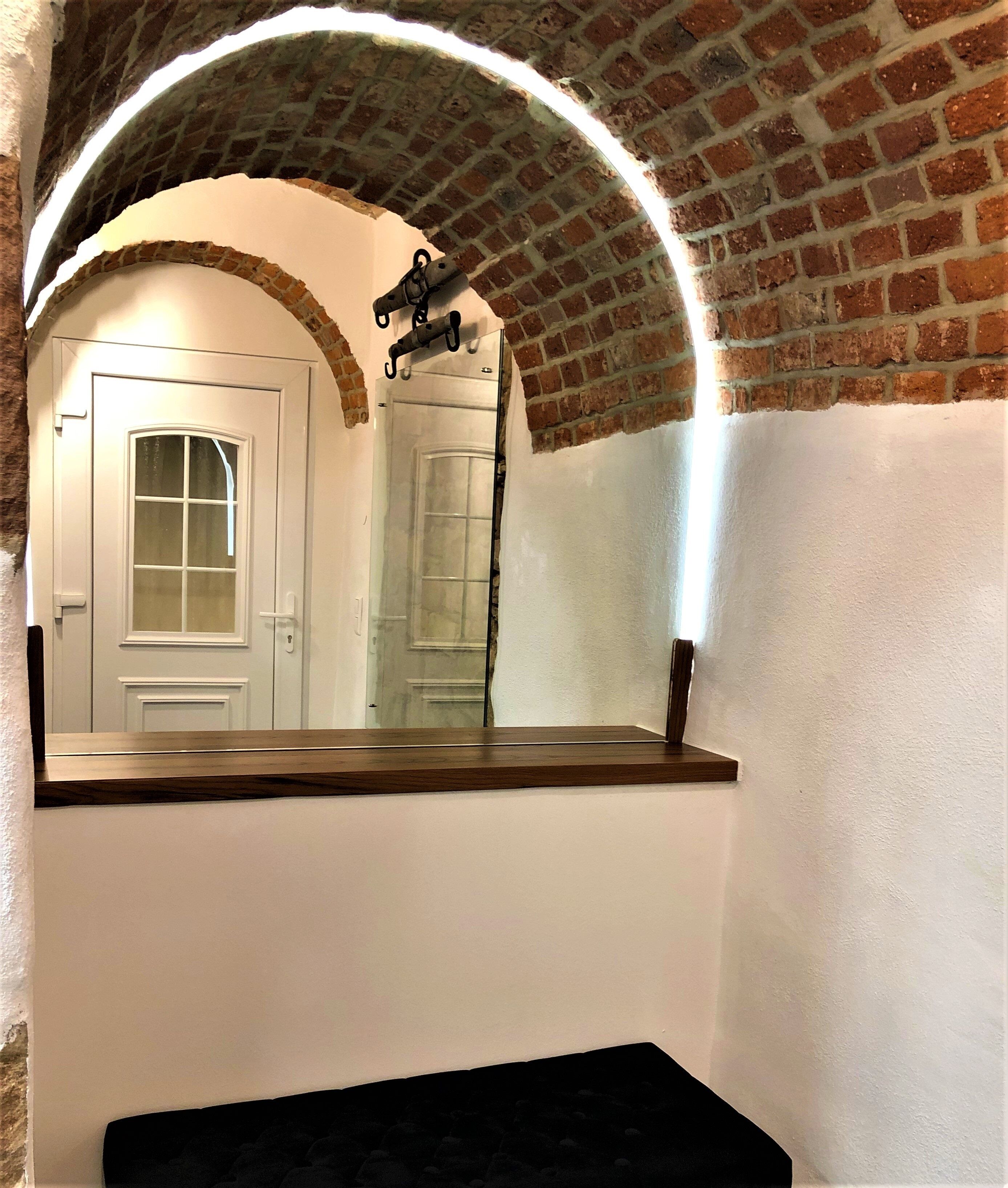 Casa de banho com porta branca, espelho e arco de tijolos.
