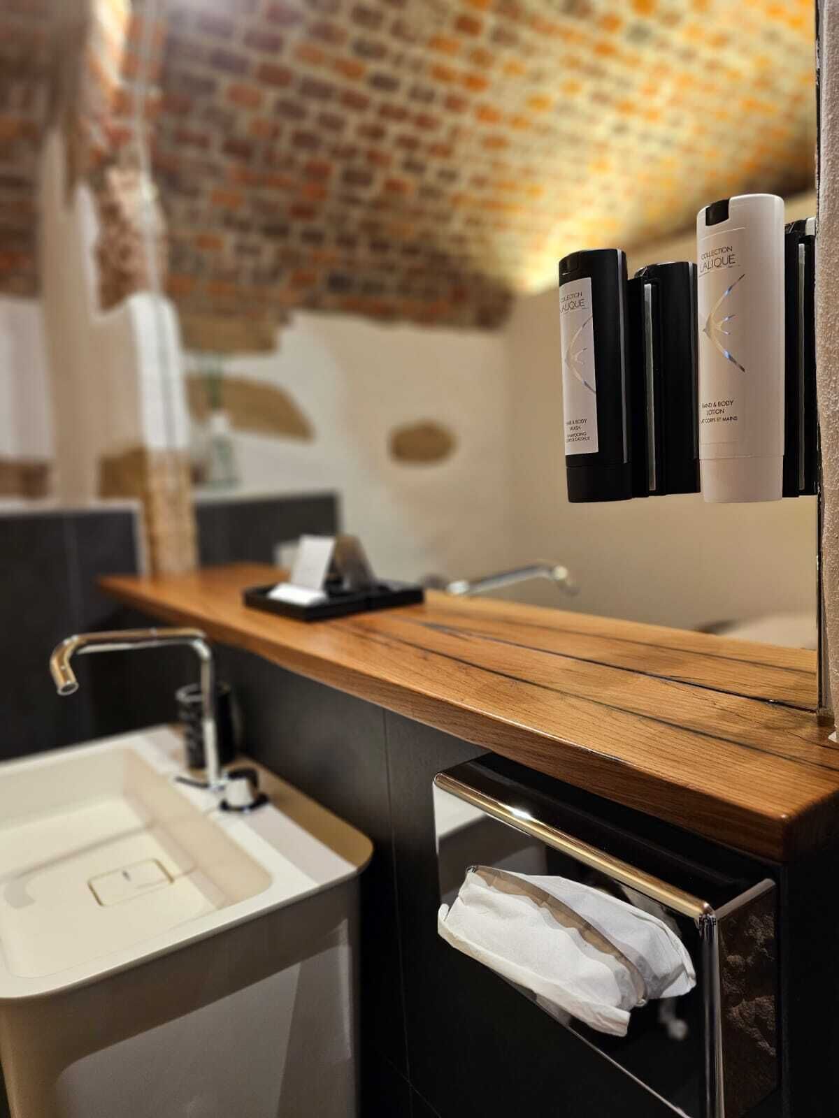 A modern bathroom with a wooden countertop, a sink, and a mirror. There are toiletries on the wall and a towel rack with a towel.