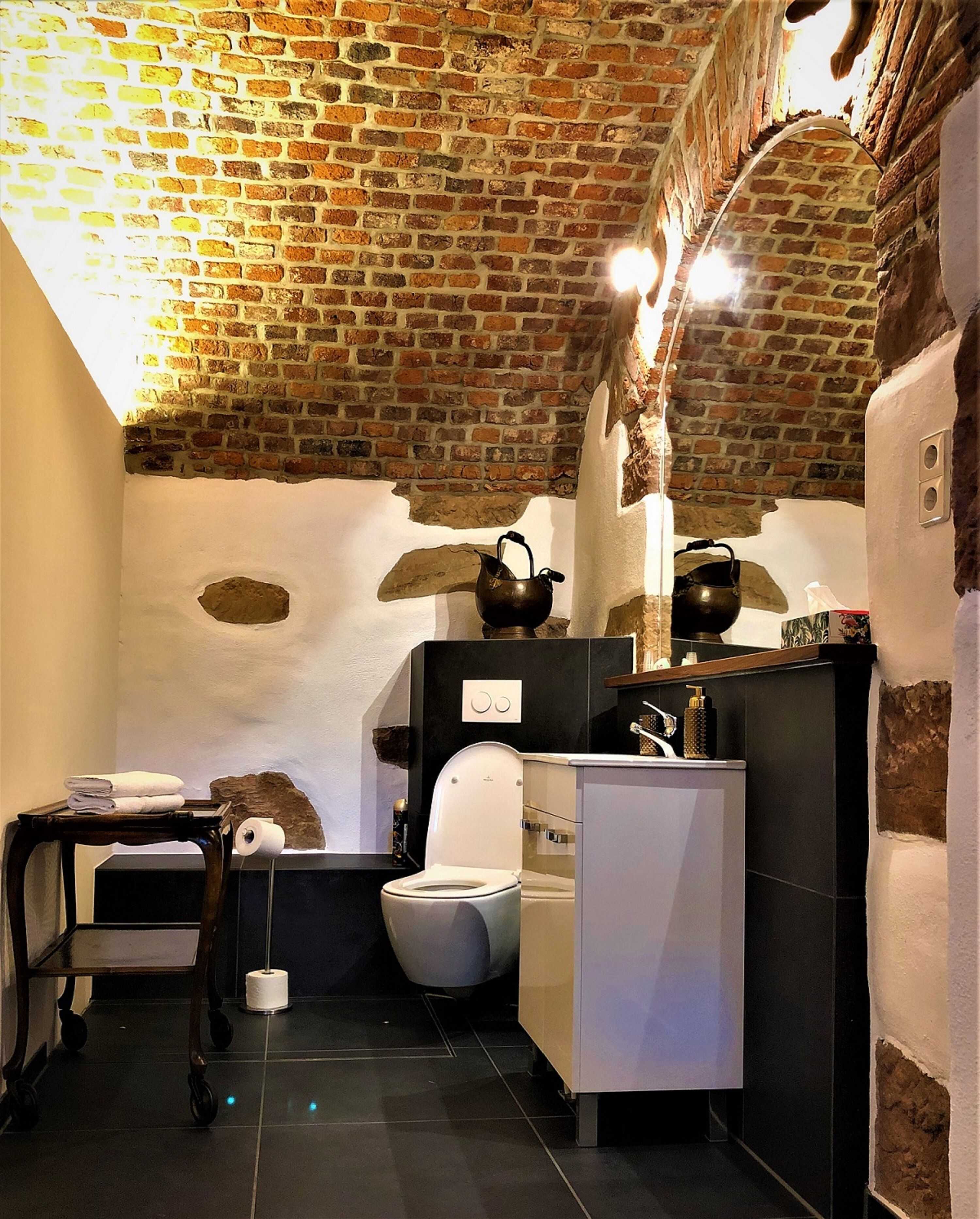 A bathroom with a rustic brick ceiling, a white toilet, a sink with a mirror, and a small table with towels.