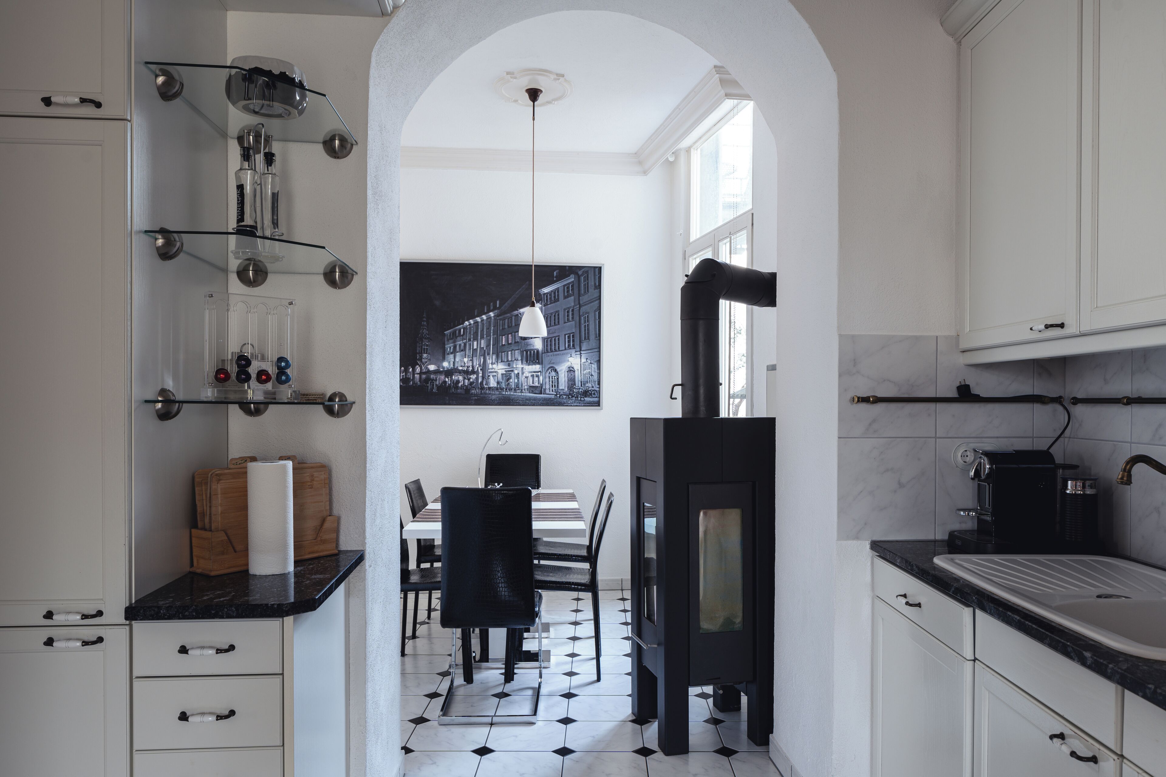 A modern kitchen with a dining area, featuring a black stove, white cabinets, and a black and white tiled floor.