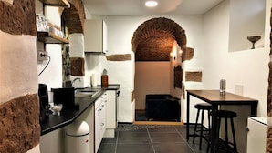 A compact kitchen with a brick archway, white cabinets, a black countertop, and a small dining area with stools.