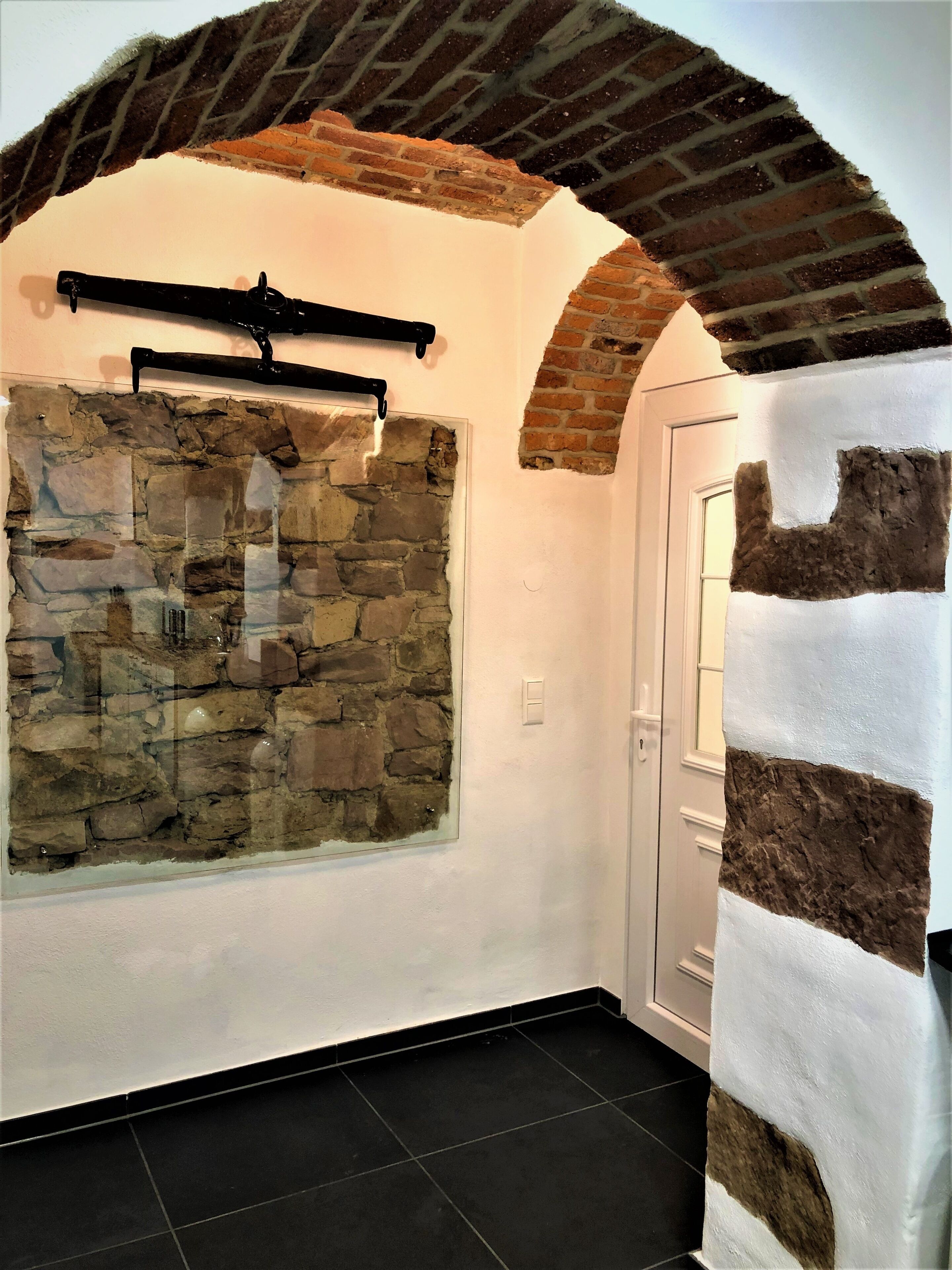 A hallway with a stone wall, a black metal rack, and a white door.