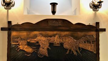 Panel de madera con un relieve que representa una escena histórica, colocado en una pared con dos apliques.