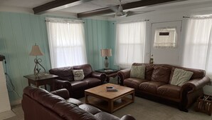 A living room with two brown leather sofas, a wooden coffee table, a lamp, and a ceiling fan. - Historic Beach Side Getaway - Pet Friendly, Wifi 3 Bedroom Cottage by RedAwning (Norfolk)