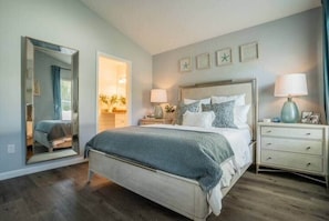 A bedroom with a bed, bedside tables, a mirror, and a wall with framed pictures.