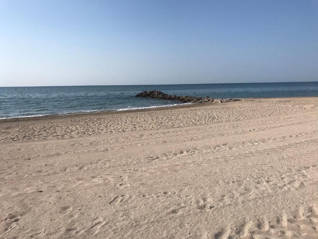 Ein sandiger Strand mit deutlichen Fußspuren und einem Felsen im Wasser.
