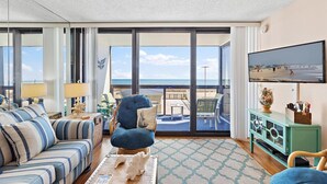 Ein Wohnzimmer mit einem großen Schiebeglasfenster, das auf einen Balkon mit Blick auf den Strand führt.