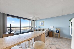 Relax in this spacious living area with a large window offering a view of the beach, a comfortable sofa, and a dining table with bar stools.