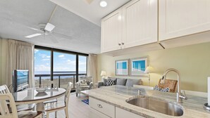 Een moderne keuken met een groot eiland, een eethoek met tafel en stoelen, en uitzicht op zee.