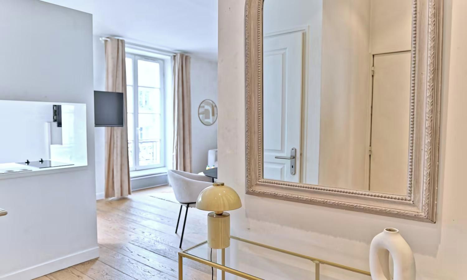 Habitación de hotel moderna con un espejo grande, televisión de pantalla plana, una silla blanca y piso de madera.