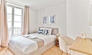 A hotel room with a bed, a bedside table, a chair, and a window with curtains. - ENCHANTING SAINT-GERMAIN HIDEAWAY:3-BEDROOM HOME STEPS FROM PARISIAN LANDMARKS (Paris)