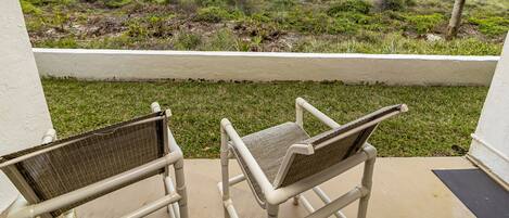 A balcony with two wicker chairs overlooking a beach with a palm tree and a white fence.