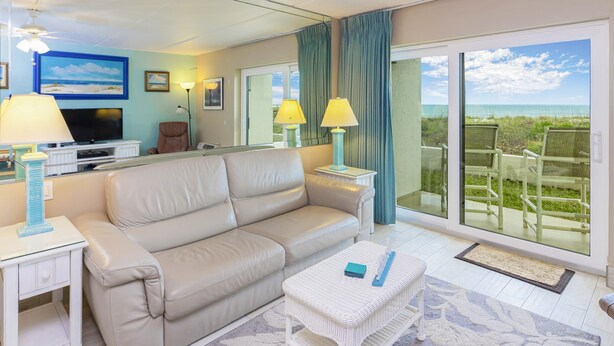 Ein modernes Wohnzimmer mit einem beigefarbenen Sofa, einem Flachbildfernseher und einem Balkon mit Meerblick.