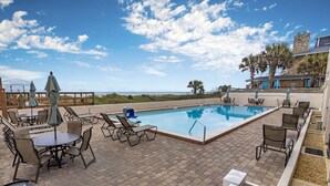 Ein Poolbereich mit Liegestühlen und Sonnenschirmen mit Blick auf einen Strand.