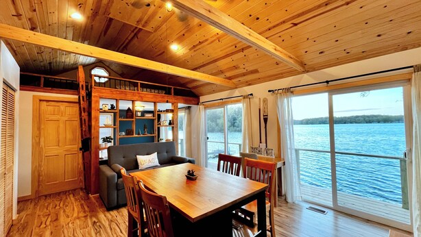 L’intérieur chaleureux d’un chalet avec une table à manger en bois, un canapé et une grande fenêtre donnant sur un lac.
