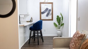 A living room with a blue chair, a beige sofa, a white vase, and a framed artwork on the wall.